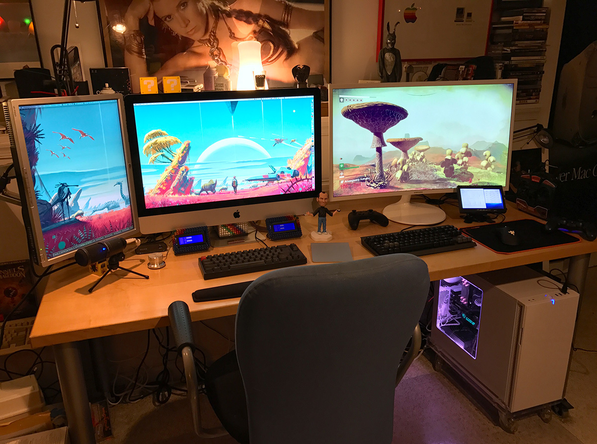 Photo of desk showing iMac on the left and gaming PC running No Man's Sky on the right